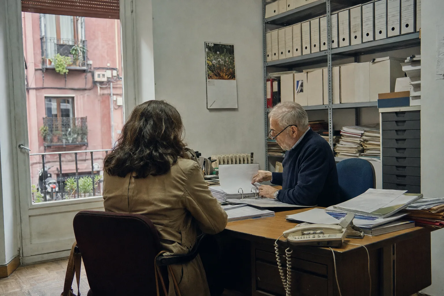 Una agente inmobiliaria, de espaldas, habla con un administrador de fincas que hojea un archivador en su despacho del centro de Valladolid.